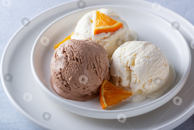Скачать Ванильно-шоколадное мороженое и дольки апельсина в тарелке на столе из светлого дерева фотосток Ozero