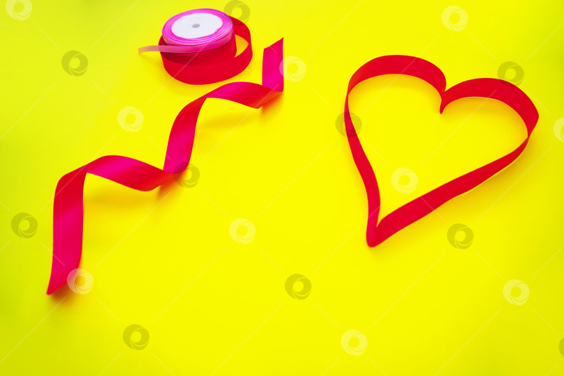 Скачать На желтом фоне - розовая атласная лента в форме сердца.Подарочная упаковка. фотосток Ozero