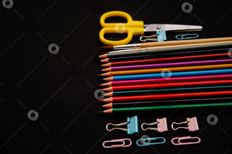 Скачать Цветные карандаши, скрепки и зажимы расположены в ряд на черном фоне. Школьные принадлежности. фотосток Ozero