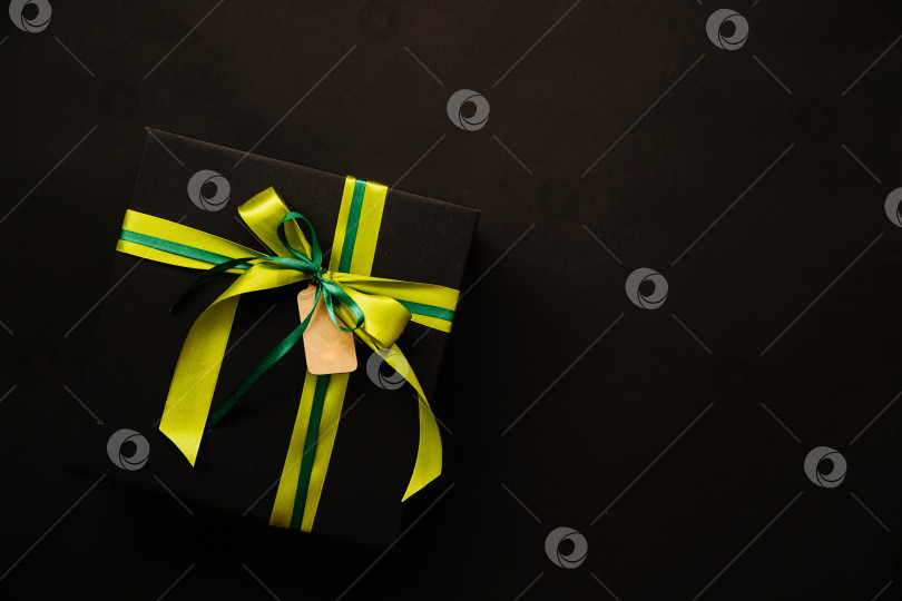 Скачать Черная подарочная коробка на черном фоне. Коробка украшена зеленой атласной лентой, завязанной бантом.Черное на черном. фотосток Ozero