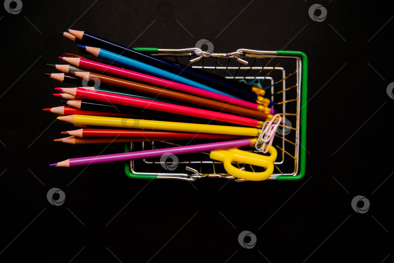Скачать Цветные карандаши расположены в ряд в продуктовой корзине на черном фоне. Школьные принадлежности. фотосток Ozero