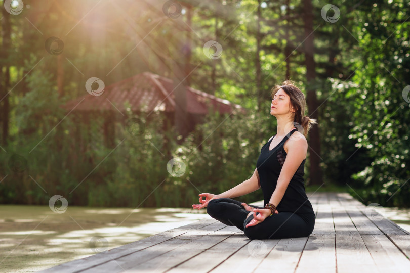 Скачать Женщина медитирует в позе лотоса на деревянной дорожке на открытом воздухе фотосток Ozero