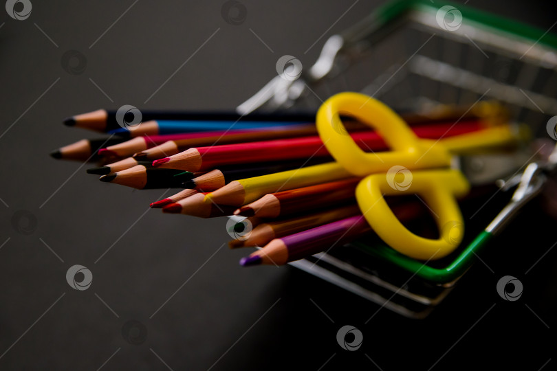Скачать Цветные карандаши расположены в ряд в продуктовой корзине на черном фоне. Школьные принадлежности. фотосток Ozero