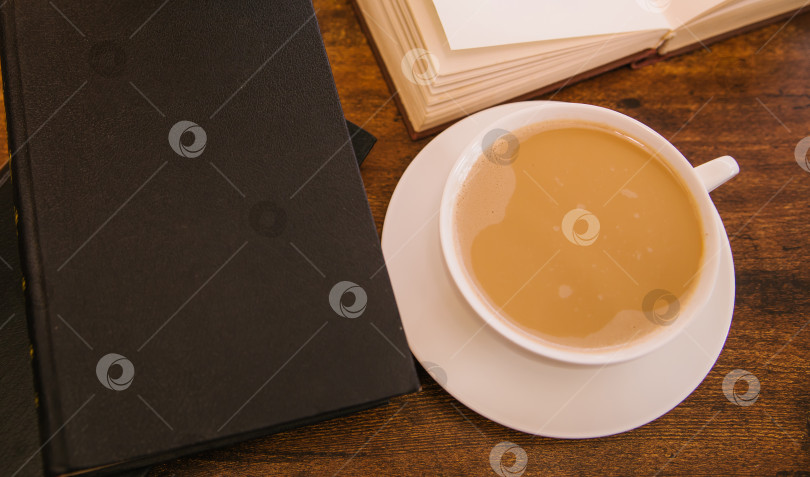 Скачать Белая чашка кофе стоит на деревянном столе. Рядом лежат книги в твердом переплете. Учебники или художественная литература. фотосток Ozero