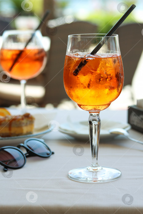 Скачать Бокал апельсинового коктейля aperol spritz или campari с долькой апельсина и льдом на столике ресторана на берегу моря в солнечный день. Концепция праздника. Летние коктейли, живое фото в отпуске фотосток Ozero