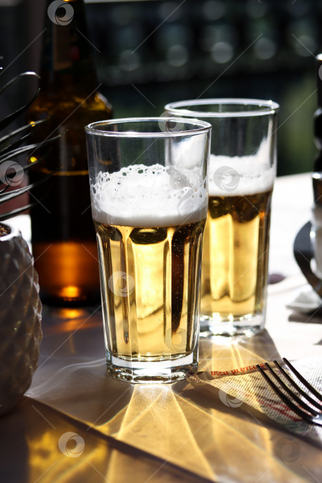 Скачать Два бокала холодного светлого пива с пенкой на столе ресторана. Фотография в реальной жизни в ресторане, солнечный день, легкое холодное пиво на столе, крупный план. фотосток Ozero