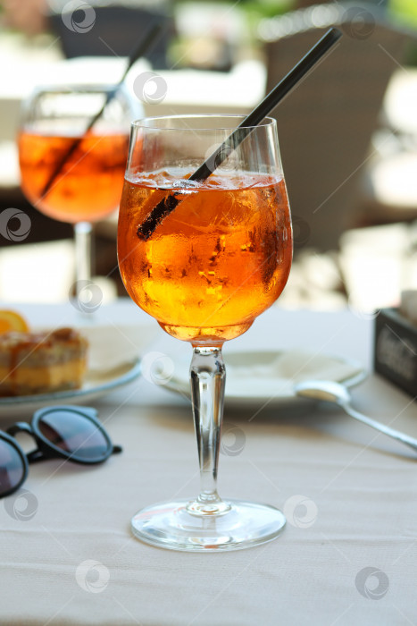 Скачать Бокал апельсинового коктейля aperol spritz или campari с долькой апельсина и льдом на столике ресторана на берегу моря в солнечный день. Концепция праздника. Летний коктейль, живое фото, отпускное настроение фотосток Ozero