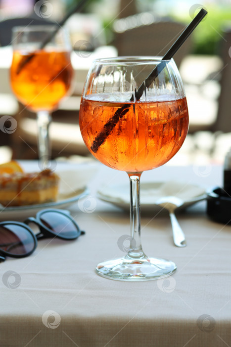 Скачать Бокал апельсинового коктейля aperol spritz или campari с долькой апельсина и льдом на столике ресторана на берегу моря в солнечный день. Концепция праздника. Летний коктейль, живое фото, крупный план фотосток Ozero