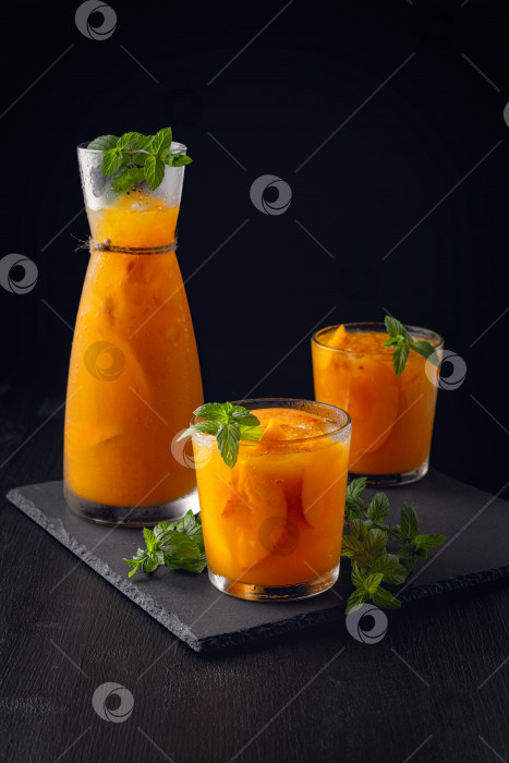 Скачать Летние холодные напитки: домашняя персиковая сангрия со льдом и мятой в бокале на черном деревянном фоне фотосток Ozero