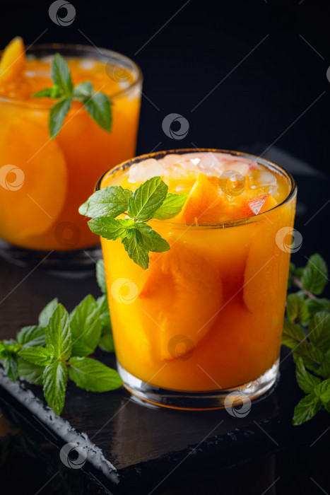 Скачать Летние холодные напитки: домашняя персиковая сангрия со льдом и мятой в бокале на черном деревянном фоне фотосток Ozero