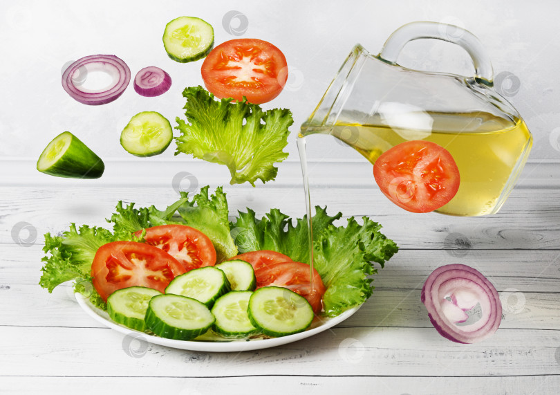 Скачать Овощной салат с оливковым маслом в "левитации". Овощной салат из помидоров, огурцов и зеленого салата с растительным маслом фотосток Ozero