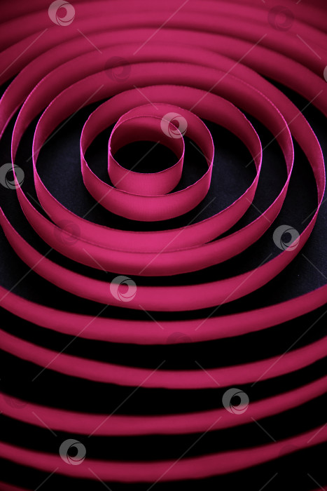 Скачать Темно-бордовая атласная лента, уложенная кругами по спирали на черном фоне. Абстрактный фон. фотосток Ozero