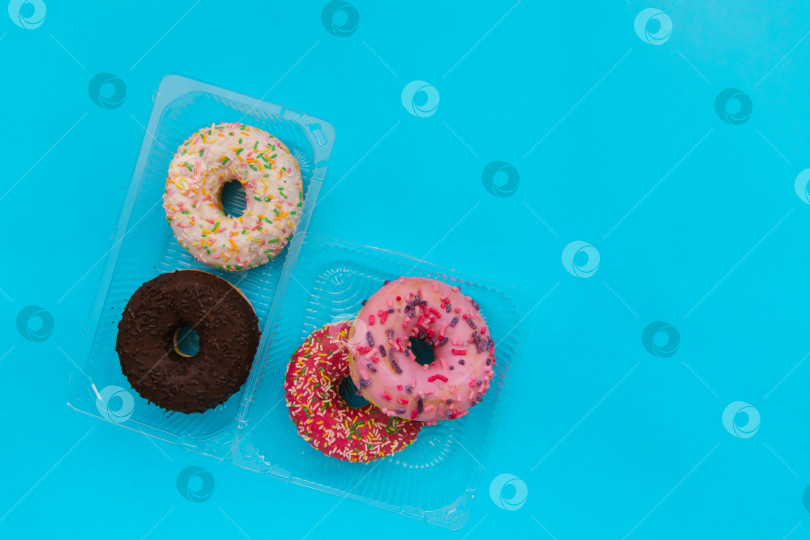 Скачать Сладкие пончики разных цветов в пластиковом контейнере на синем фоне. Кондитерские изделия. фотосток Ozero