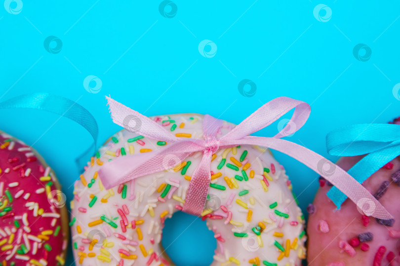 Скачать Сладкие пончики разных цветов расположены в ряд на синем фоне. фотосток Ozero