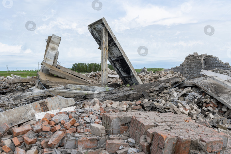 Скачать Остатки только что разобранного сельскохозяйственного здания или сооружения на фоне летнего пейзажа. На земле лежат железобетонные плиты перекрытия и кирпичная крошка. фотосток Ozero