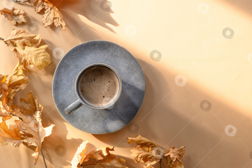 Скачать Кофе в серой чашке и сухие дубовые листья на бежевом фоне. фотосток Ozero