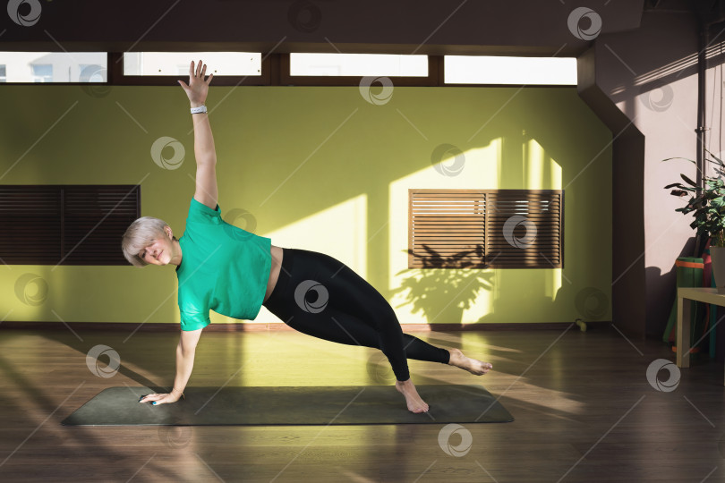 Скачать Женщина, ведущая здоровый образ жизни и практикующая йогу, выполняет упражнение васиштхасана, позу боковой доски, тренируется на коврике в студии фотосток Ozero