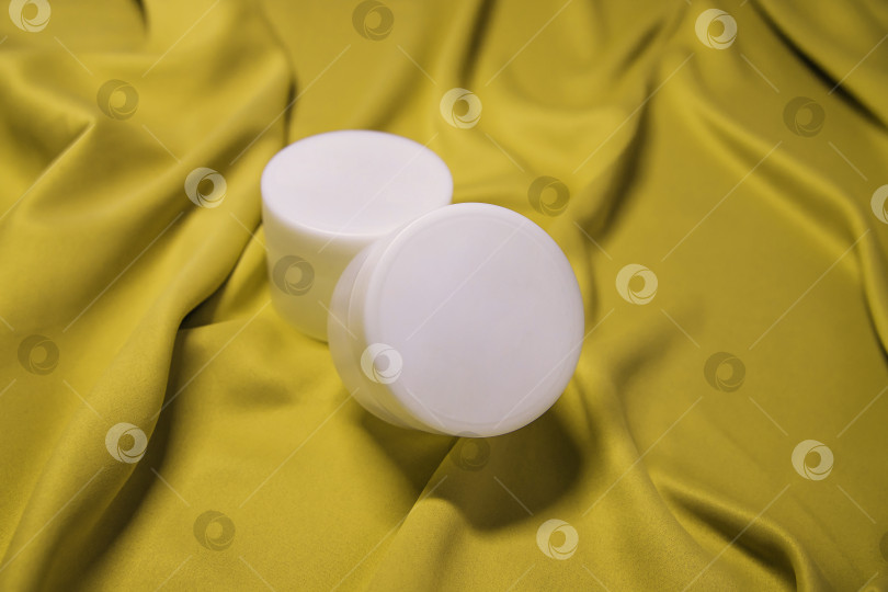 Скачать Пустая белая пластиковая баночка с кремом или гелем. Закрытая круглая банка на фоне желтой ткани. фотосток Ozero