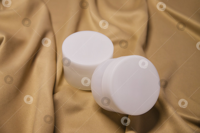 Скачать маленькая белая пластиковая баночка с кремом или гелем. Закрытая круглая банка на фоне бежевой ткани. фотосток Ozero