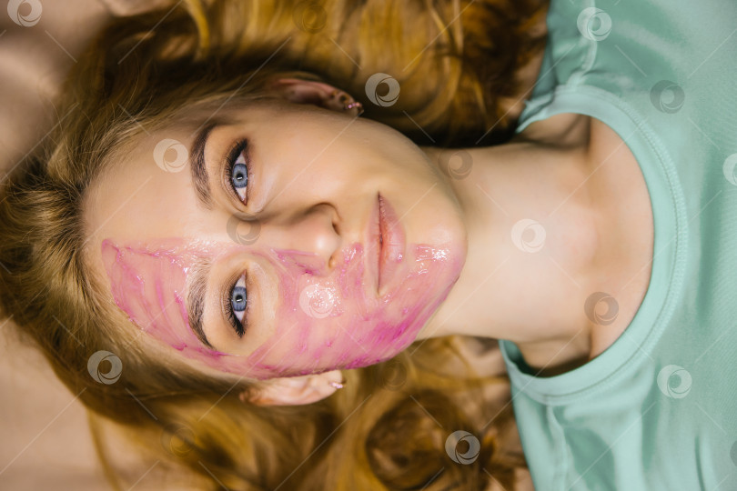 Скачать молодая женщина с розовой косметической маской на лице. Уход за кожей лица. фотосток Ozero