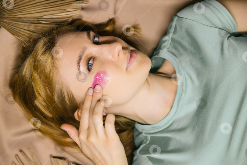 Скачать Молодая женщина наносит на лицо розовую косметическую маску или гель. Уход за кожей лица. фотосток Ozero