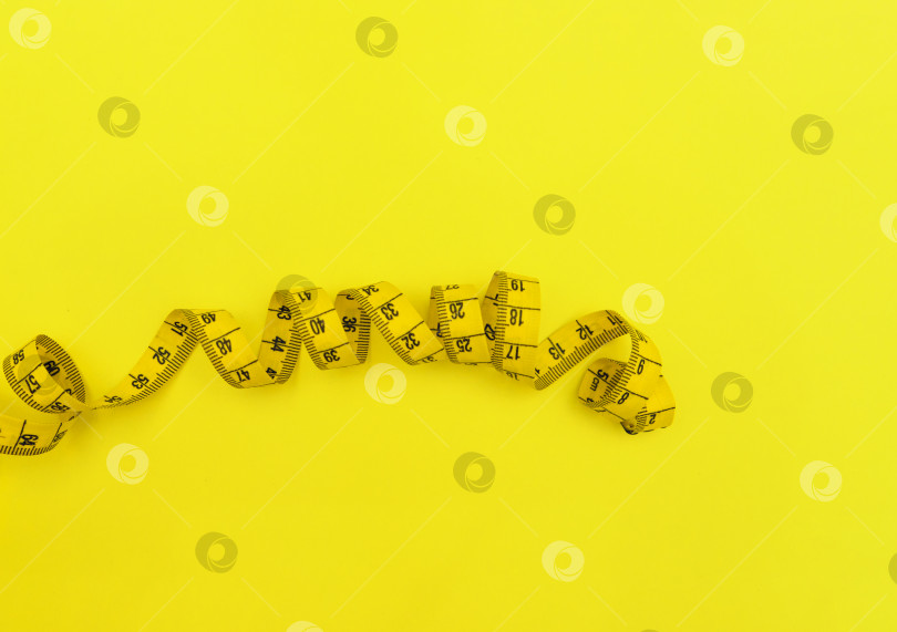 Скачать Сантиметровая лента желтого цвета на желтом фоне. Инструмент для измерения расстояний. фотосток Ozero