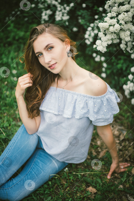 Скачать Молодая женщина сидит на траве возле красивого куста с белыми цветами.Весенний портрет красивой девушки. фотосток Ozero