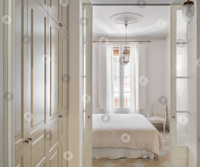 Скачать Вид на светлый интерьер спальни, совмещенный с гардеробной зоной, оформленной в винтажном стиле. фотосток Ozero