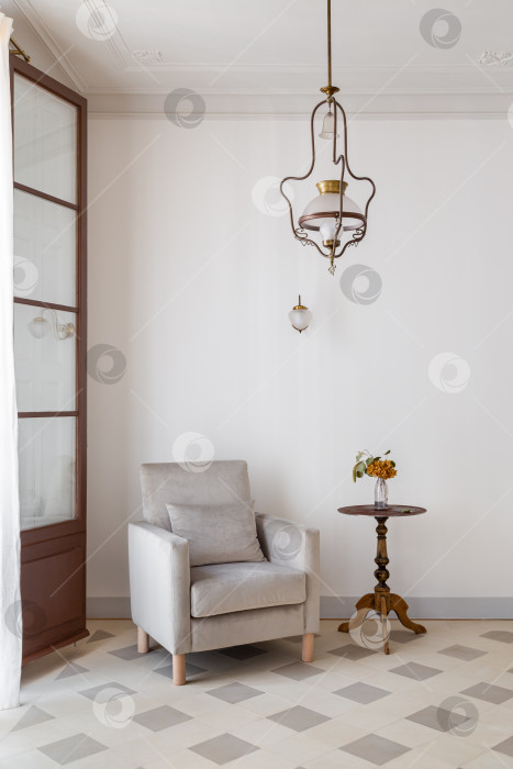 Скачать Интерьер гостиной с уютным креслом и приставным столиком у белой стены. Ретро-стиль с винтажной люстрой. фотосток Ozero