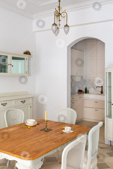 Скачать Деревянный обеденный стол на две персоны в классической гостиной, оформленной в стиле ретро, с видом на кухню. фотосток Ozero