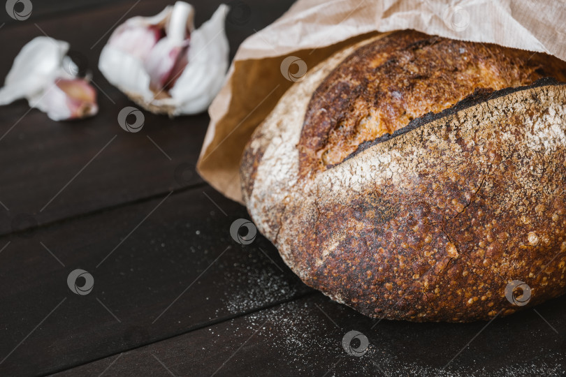 Скачать Крупный план хрустящего круглого хлеба на закваске из цельного зерна в крафтовой упаковке с чесноком. Концепция натурального и здорового питания. фотосток Ozero