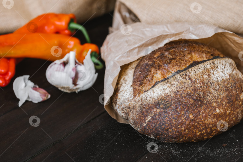 Скачать Хлеб на закваске ручной работы на деревянном столе с овощами. Свежеиспеченный круглый батон хлеба на закваске фотосток Ozero