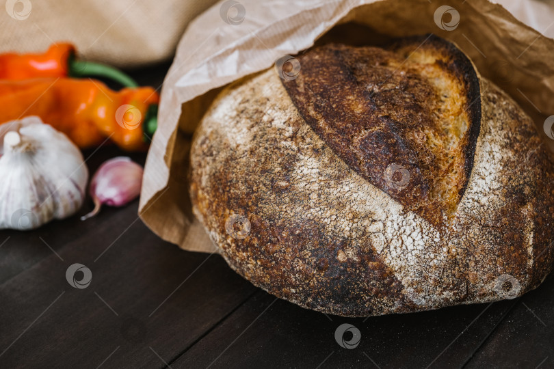 Скачать Свежеиспеченный круглый батон хлеба на закваске на деревянном столе с овощами. Хлеб на закваске ручной работы. фотосток Ozero