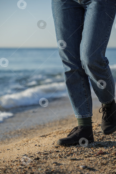 Скачать Женщина в синих джинсах и черных туфлях прогуливается по пляжу на фоне морских волн фотосток Ozero