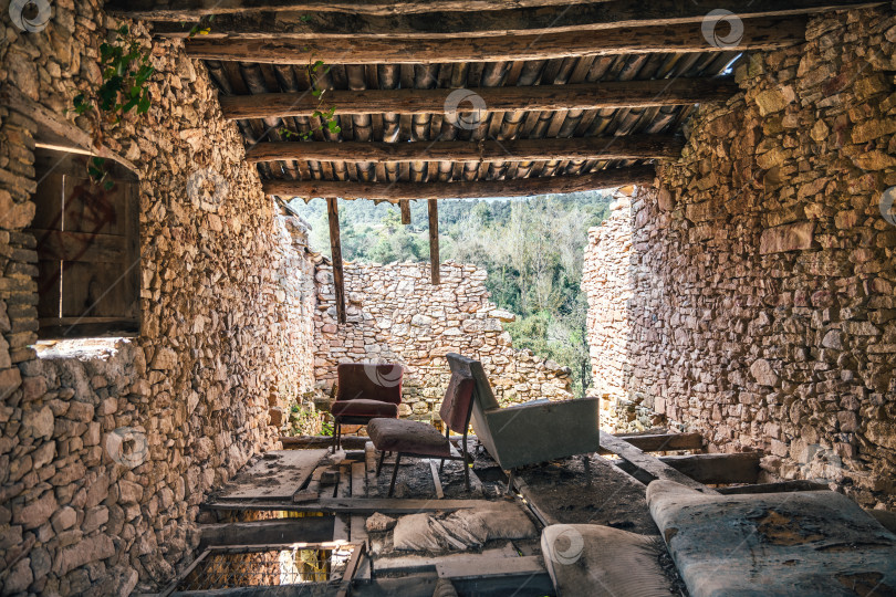 Скачать Заброшенный каменный дом с деревянной крышей и разрушенной стеной с видом снаружи. Руины древнего заброшенного здания со старой мебелью. фотосток Ozero