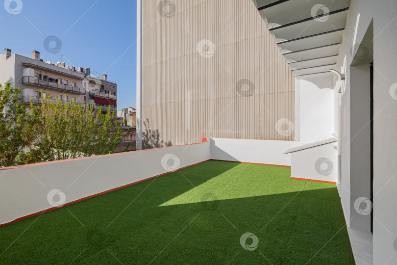Скачать Пустая солнечная терраса отремонтированной квартиры с газоном из искусственной зеленой травы. Вид на улицу и голубое небо в центре Барселоны фотосток Ozero