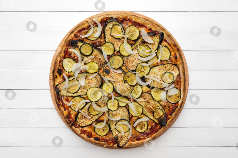Скачать Цельнозерновая вегетарианская пицца с баклажанами, цуккини и луком-гриль на деревянной тарелке. Вид сверху на фоне белой доски фотосток Ozero