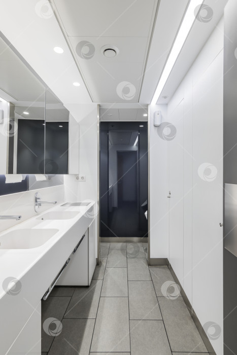Скачать Общественный или офисный интерьер мужского туалета с раковинами и большим зеркалом. Ванная комната современного дизайна в белом цвете. фотосток Ozero