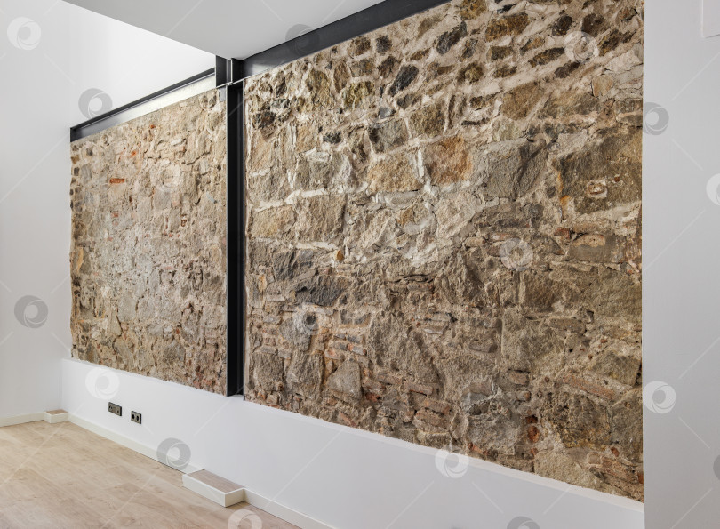 Скачать Восстановленная древняя стена, оставшаяся от зданий старого города в Барселоне. Интерьер пустой отремонтированной квартиры с каменной стеной. фотосток Ozero