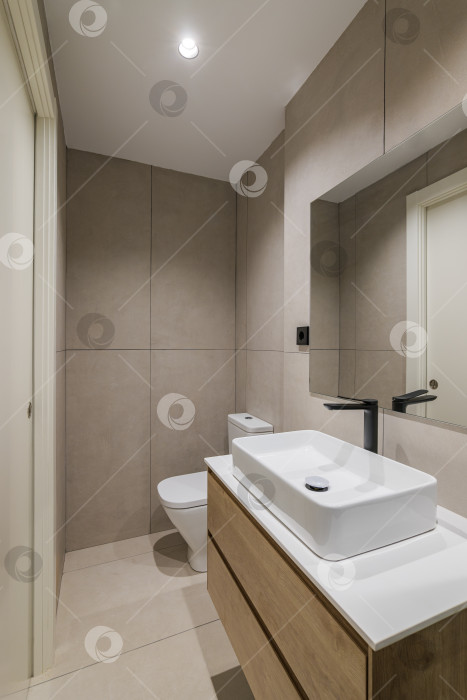 Скачать Интерьер ванной комнаты в современном стиле в отремонтированной квартире. Узкий унитаз с раковиной, черным краном и зеркалом. фотосток Ozero