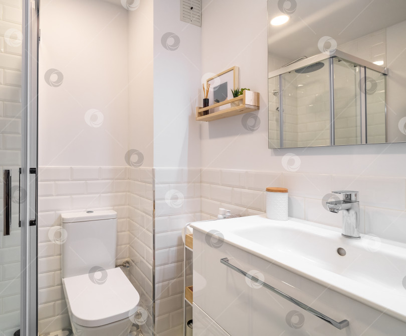 Скачать Современная ванная комната с белой керамической плиткой и отражающейся в зеркале душевой кабиной. фотосток Ozero