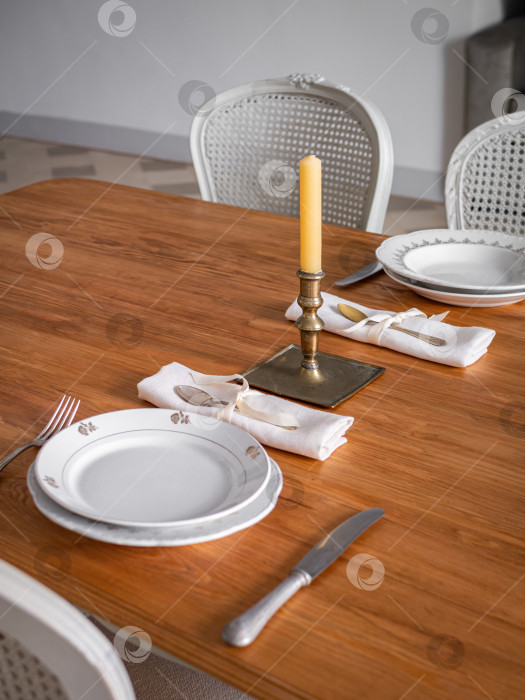 Скачать Деревянная сервировка стола на две персоны, с тарелками, столовыми приборами и старинным подсвечником со свечой. Интерьер гостиной оформлен в винтажном стиле. фотосток Ozero