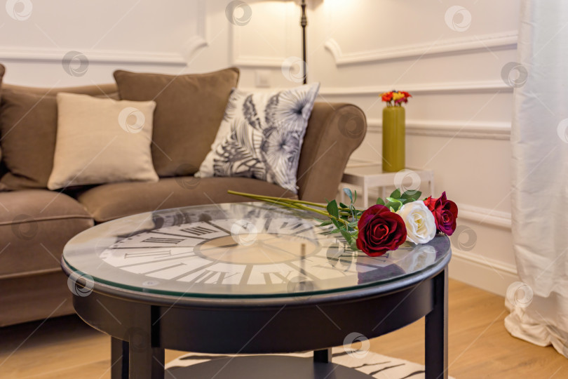 Скачать Свежие розы на журнальном столике с часами внутри. Интерьер гостиной с уютным диваном. фотосток Ozero