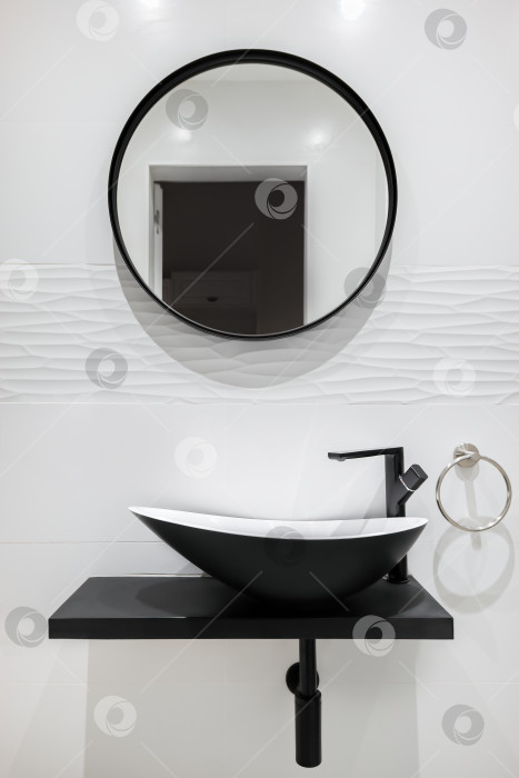 Скачать Ванная комната, выложенная белым кафелем, с черным краном, раковиной и круглым зеркалом. Современный и минималистский стиль. фотосток Ozero