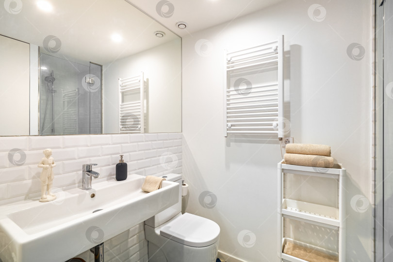 Скачать Интерьер белой ванной комнаты в отремонтированной квартире. Душевая зона с обогревателем, раковиной и зеркалом фотосток Ozero