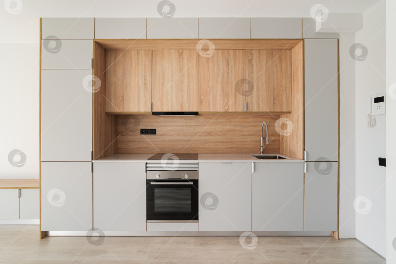 Скачать Современная кухня в стиле минимализма в пустой отремонтированной квартире. Деревянная мебель и современная бытовая техника фотосток Ozero
