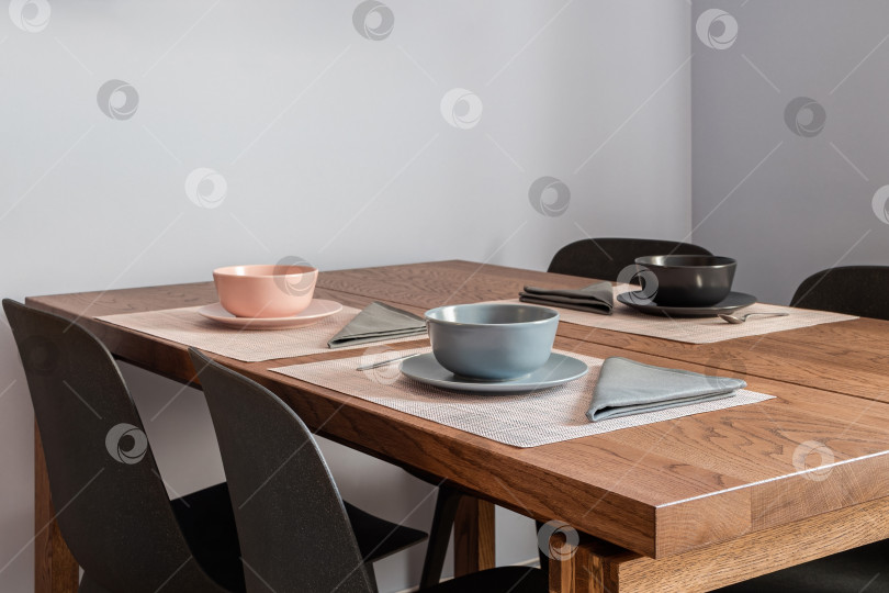Скачать Стильный интерьер столовой с деревянным столом, накрытым на три персоны, с мисками и столовыми приборами фотосток Ozero