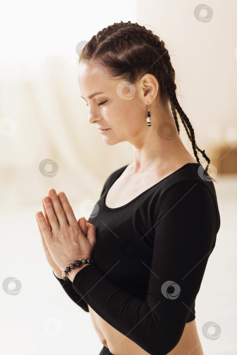 Скачать Портрет женщины в спортивной одежде, практикующей йогу и выполняющей медитацию с намасте у груди, стоя в студии фотосток Ozero