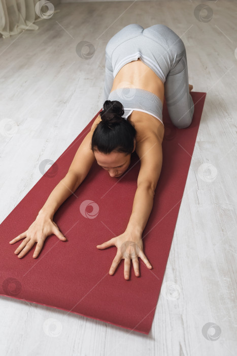 Скачать Женщина, практикующая йогу, выполняет упражнение баласана со средним раскрытием бедер, поза ребенка, она тренируется на коврике в студии фотосток Ozero