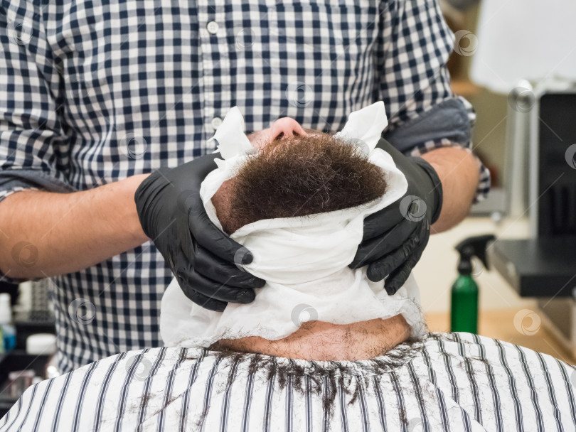 Скачать Парикмахер прикладывает теплое полотенце к лицу мужчины перед тем, как побрить его в парикмахерской. фотосток Ozero
